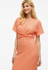 Robe tricotée orange à manches courtes, avec un détail central torsadé et un motif texturé sur l'ensemble du tissu.