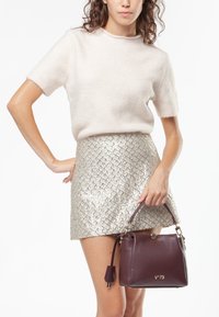 Bordeaux leren handtas met een gestructureerde vorm, gouden accenten en een afneembare schouderband. Zachte beige korte mouwen trui en metalen rok.