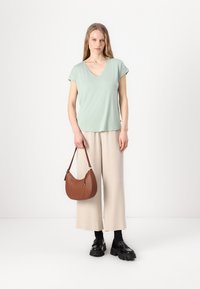 Tricou v-neck verde mentă, pantaloni crem cu croială largă, geantă din piele maro cu formă curbată și mocasini negri cu talpă din cauciuc.