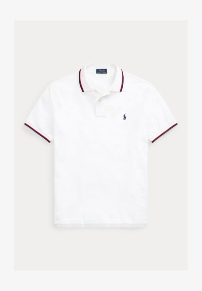 Polo branca com gola riscada em vermelho e azul-marinho, mangas curtas, pala com três botões e logótipo azul-marinho bordado no peito esquerdo.