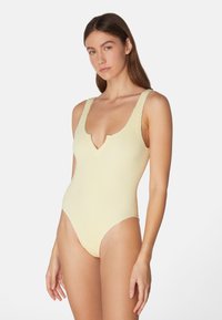 Gul ribbad baddräkt i ett stycke med rundad halsringning och låg rygg. Har tjocka axelremmar och högskurna ben, tillverkad av strukturerat material.