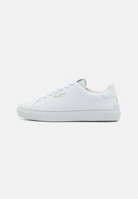 Zapatilla de cuero blanca con punta redonda, seis ojales, detalle del logo en dorado y suela de goma texturizada. Diseño limpio con acentos mínimos.