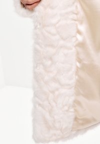 Abrigo de fieltro sintético en rosa claro con una textura suave. Forro de satén en un suave beis. Presenta un acabado liso y sutiles detalles de costura.