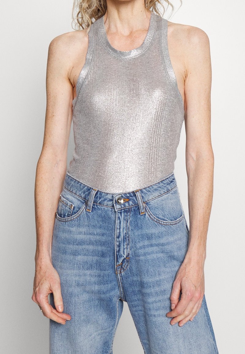 Top tank metálico plateado con textura acanalada, cuello alto y diseño sin mangas, combinado con jeans de talle alto azul claro.
