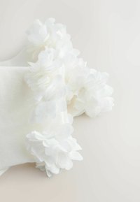 Fehér zokni texturált bordázott mintával, a szárán fehér szövetvirágokkal díszítve, amelyek dimenziós részletet és puhaságot kölcsönöznek.