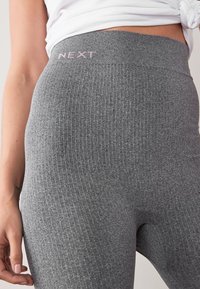 Leggings côtelés gris avec une taille haute arborant le logo "NEXT" en rose. La texture est douce et extensible pour un confort optimal.