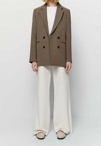 Blazer marrone doppiopetto con una vestibilità strutturata, abbinato a pantaloni bianchi a gamba larga e scarpe beige slip-on.