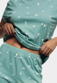 Conjunto de loungewear de algodón turquesa que incluye una camiseta de manga corta y pantalones cortos con cintura elástica. Decorado con pequeños patrones de corazones blancos en todo el conjunto.