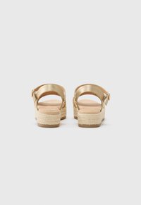 Gold strappy sandals with a platform. Features braided jute detailing, an ankle strap with a buckle, and a smooth, matte finish.