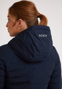 Giacca puffer blu navy con cappuccio, caratterizzata da una finitura opaca, cuciture visibili e "JACK1T" ricamato in argento sul retro.