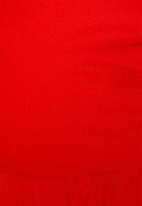 O tecido vermelho apresenta uma superfície texturizada com sutis nervuras e uma bainha com volantes em camadas na parte inferior, exibindo um acabamento vibrante e suave.