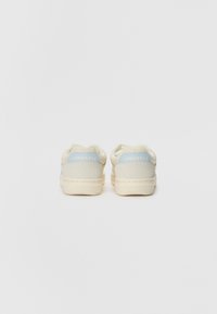 White leather sneakers with light blue accents, round toe, and textured heel tabs featuring the "Converse" logo. Smooth sole; minimal design.