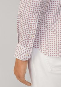 Witte shirt met een klein geometrisch patroon in rood en bruin, met een knoopmanchet en een fijne stofstructuur.