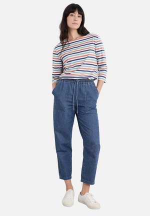 Camicia a maniche lunghe a righe bianca, blu, rossa e verde; pantaloni jogger in denim blu con cintura elastica e due tasche frontali; sneakers bianche.