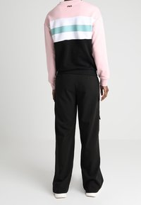 Różowa i czarna bluza kolor-block z trzema poziomymi paskami w białym i turkusowym kolorze; zestawiona z czarnymi spodniami typu wide-leg i białymi trampkami.