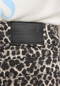 Close-up of leopard print pants with black stitched leather patch reading "America Today" near waistline under a white shirt.