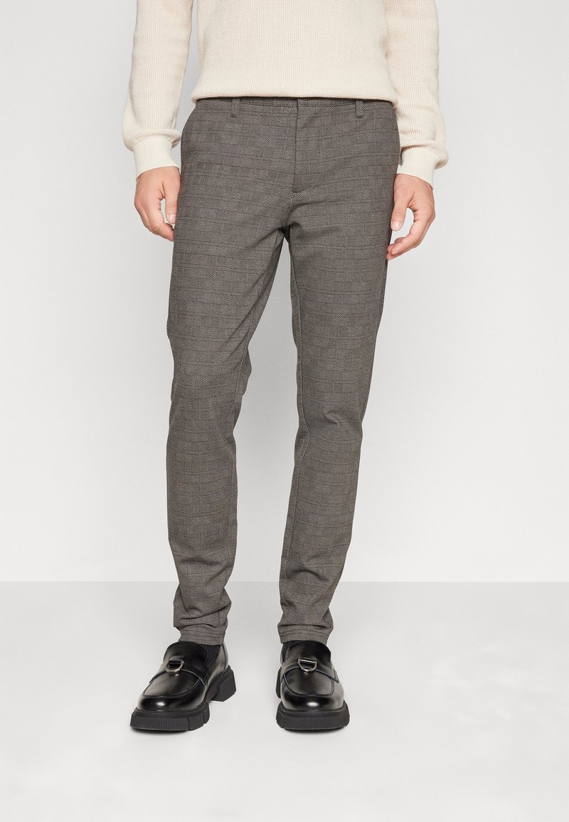 Pantalon gris à carreaux, coupe slim, présentant une texture subtile, des poches latérales et un devant plat. Associé à des chaussures noires.