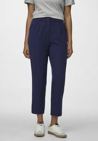 Tumši zili šauri bikses ar priekšējo krokām, pogu aizdari un sānu kabatām, saskaņotas ar baltām kedām ar pelēkām akcentiem.