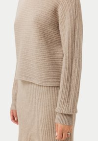 Beige stickad tröja och kjolset, med ribbad textur, cropped design och lång ärm med vida manschetter. Materialet är mjukt.