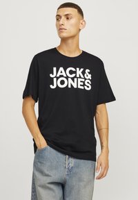 T-shirt negru din bumbac, cu text alb, îndrăzneț "JACK & JONES". Mâneci scurte și o croială lejeră, asortat cu jeanși din denim albastru deschis.