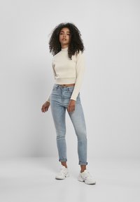Krämfärgad crop-tröja med långa ärmar, ihop med ljusblå tapered jeans och vita sportskor. Outfiten har en avslappnad passform.