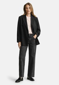 Schwarzer, doppelt gefütterter Blazer über einem rosa T-Shirt, kombiniert mit hochtaillierten dunkelblauen Jeans und schwarzen Slippern. Glattes Material mit maßgeschneidertem Design.