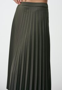 Olivgrüner, gefalteter Rock mit einem figurbetonten Bund, aus glattem Stoff gefertigt, mit vertikalen Streifen und einem langen Design.