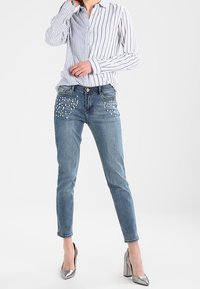Camicia button-up a righe, jeans in denim chiaro con decorazioni in perle sul davanti e scarpe col tacco alto argentate. Look minimale e casual.