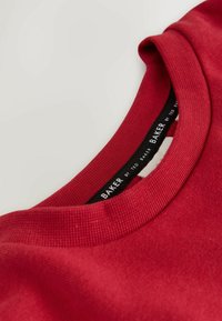 Red crew neck sweatshirt made of smooth fabric with a ribbed collar and a tag displaying "BAKER by TED BAKER" in black text.