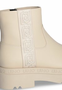 Stivaletto in finta pelle beige con pannello laterale stampato con logo argento, suola spessa con dettagli del logo e design senza cuciture.