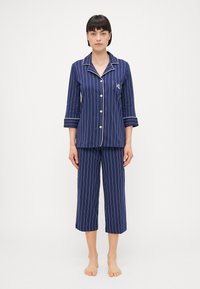 Conjunto de pijama listrado em azul-marinho, com uma camisa de botões de mangas três-quartos e calças cropped combinando; inclui detalhes brancos e um bolso.