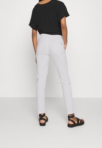 Pantalones blancos ajustados con bolsillos traseros, combinados con una blusa negra holgada y sandalias negras con tiras. Tela suave con un diseño limpio.