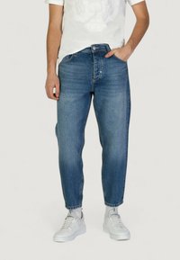 Jeans in denim blu con gamba affusolata, design a cinque tasche, leggera scoloritura e cuciture a contrasto, abbinati a una t-shirt bianca e sneakers bianche.