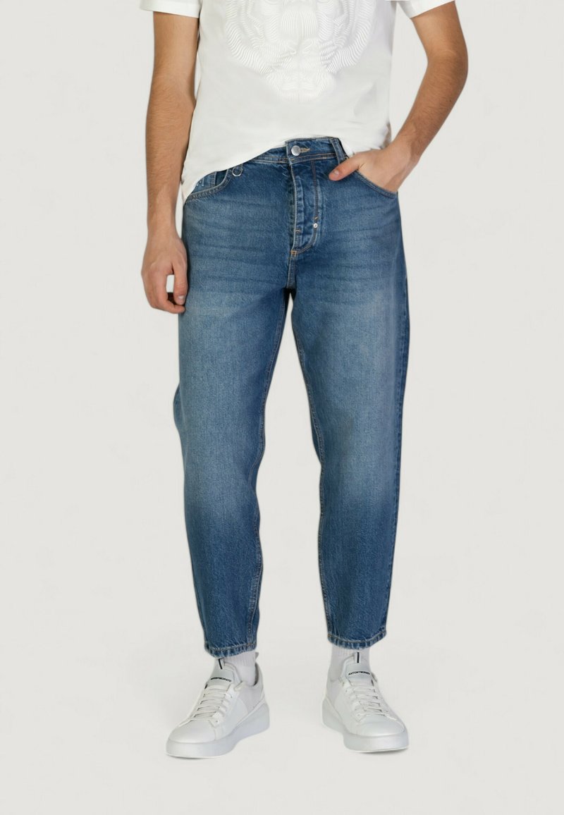 Jeans in denim blu con gamba affusolata, design a cinque tasche, leggera scoloritura e cuciture a contrasto, abbinati a una t-shirt bianca e sneakers bianche.
