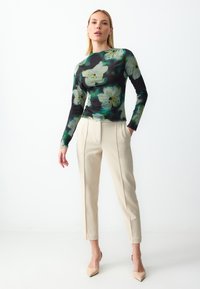 Haut à manches longues avec un fond noir orné de motifs floraux verts et blancs, associé à un pantalon beige ajusté et des escarpins nude.