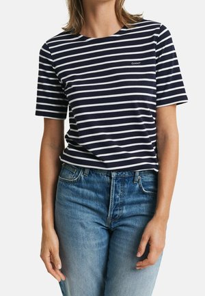 Marineblau-weiß gestreiftes T-Shirt mit kurzen Ärmeln und Rundhalsausschnitt. Verfügt über ein kleines Logo auf der Brust und ist mit Jeans kombiniert.