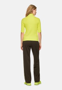 Short-sleeve, high-neck top in bright yellow, paired with loose, dark brown trousers. Bright sneakers complement the overall look.