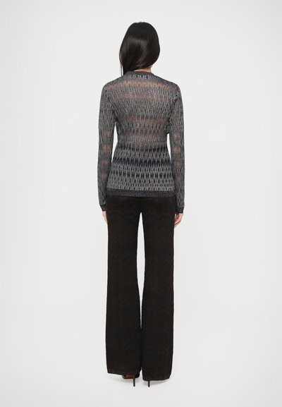Áttetsző, szürke hosszú ujjú felső cikk-cakk mintával, fekete, texturált, bőszárú nadrággal párosítva. A részletes kötésminta és a testhezálló sziluett kiemelése.
