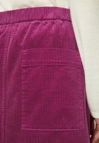 Jupe en velours côtelé fuchsia présentant une texture rayée verticale, une taille élastique et une grande poche appliquée sur la hanche.