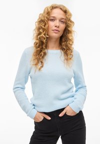 Ανοιχτό μπλε πλεκτό πουκάμισο με υφή σχέδιο, στρογγυλή λαιμόκοψη και ριμπ μανσέτες, συνδυασμένο με μαύρο παντελόνι. Κανονική εφαρμογή, μακριά μανίκια.