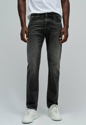 Vaqueros de mezclilla gris oscuro con corte recto, presentan un botón azul, cinco bolsillos y un ligero desvanecimiento. Combinados con zapatillas blancas.