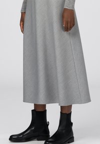 Harmaa, polven pituinen A-linjainen hame teksturoidussa kankaassa, paritettu mustien nilkkureiden kanssa, joissa on sileä pinta ja vetotappi.