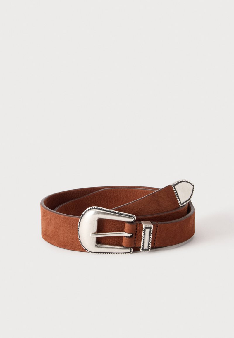 Ceinture en daim marron enroulée avec une grande boucle en métal argenté et une extrémité argentée assortie sur un fond uni clair.
