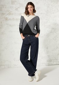 Grau, schwarz und cremefarbener, farblich blockierter Strickpullover mit gerippter Textur, kombiniert mit dunkelblauen, weit geschnittenen Jeans und weißen Sneakern.