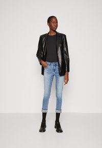 Blazer di pelle nera su una maglia nera aderente, abbinato a jeans cropped azzurri chiari con polsini decorati e scarpe nere con tacco.