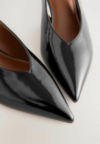 Schwarze Lackleder-Spitzenzehenschuhe mit einem V-Ausschnitt-Design, das eine glatte Oberfläche und eine braune Innenausstattung aufweist.