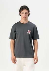 Grijs katoenen t-shirt met korte mouwen, voorzien van een grafisch ontwerp van een roze en rode hibiscusbloem op de linkerborst. Recht gesneden ontwerp.