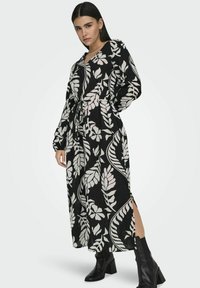 Musta pitkä mekko, jossa on kerma-valahtelukuvio, pitkät hihat ja vyötärölle sidottava nauha. Mekossa on sivurei'itykset ja se on yhdistetty mustiin korkokenkiin.