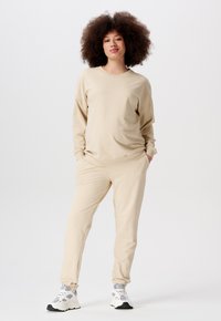 Beige loungewear set met een langemouw top en elastische broek, gemaakt van zachte stof. Gecombineerd met witte en grijze sportschoenen.