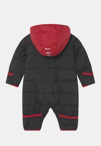 Tute invernale imbottito nero con cappuccio rosso, caratterizzato da una superficie liscia, cuciture orizzontali, dettagli rossi su polsini e gambe, e un logo sul cappuccio.